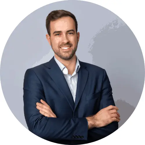 Mitch Miller, ENA. Tummansiniseen pukuun pukeutunut mies seisoo kädet ristissä ja hymyilee kameralle. Taustalla on harmaa tausta.