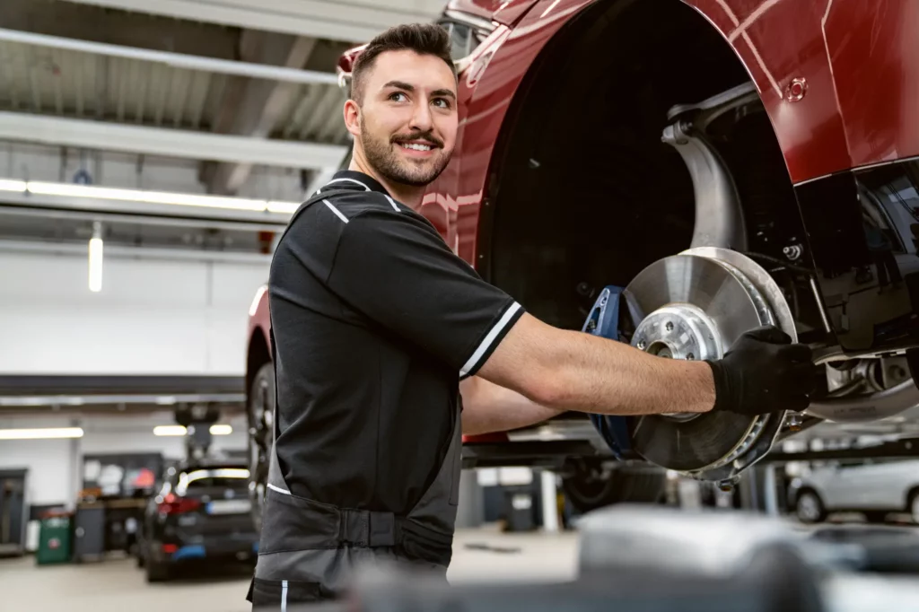 Automekaanikko työskentelee korjaamolla säätäen ripustetun auton pyöränakselia.